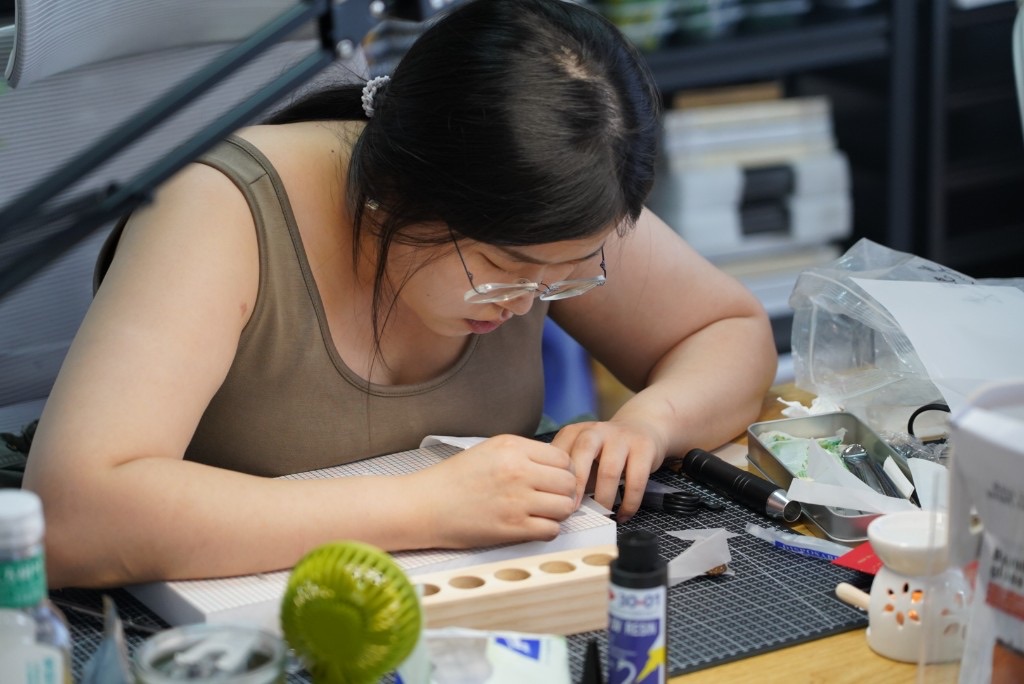 戴眼镜的工坊伙伴在工位前专注作业，桌上摆放滴胶与工具